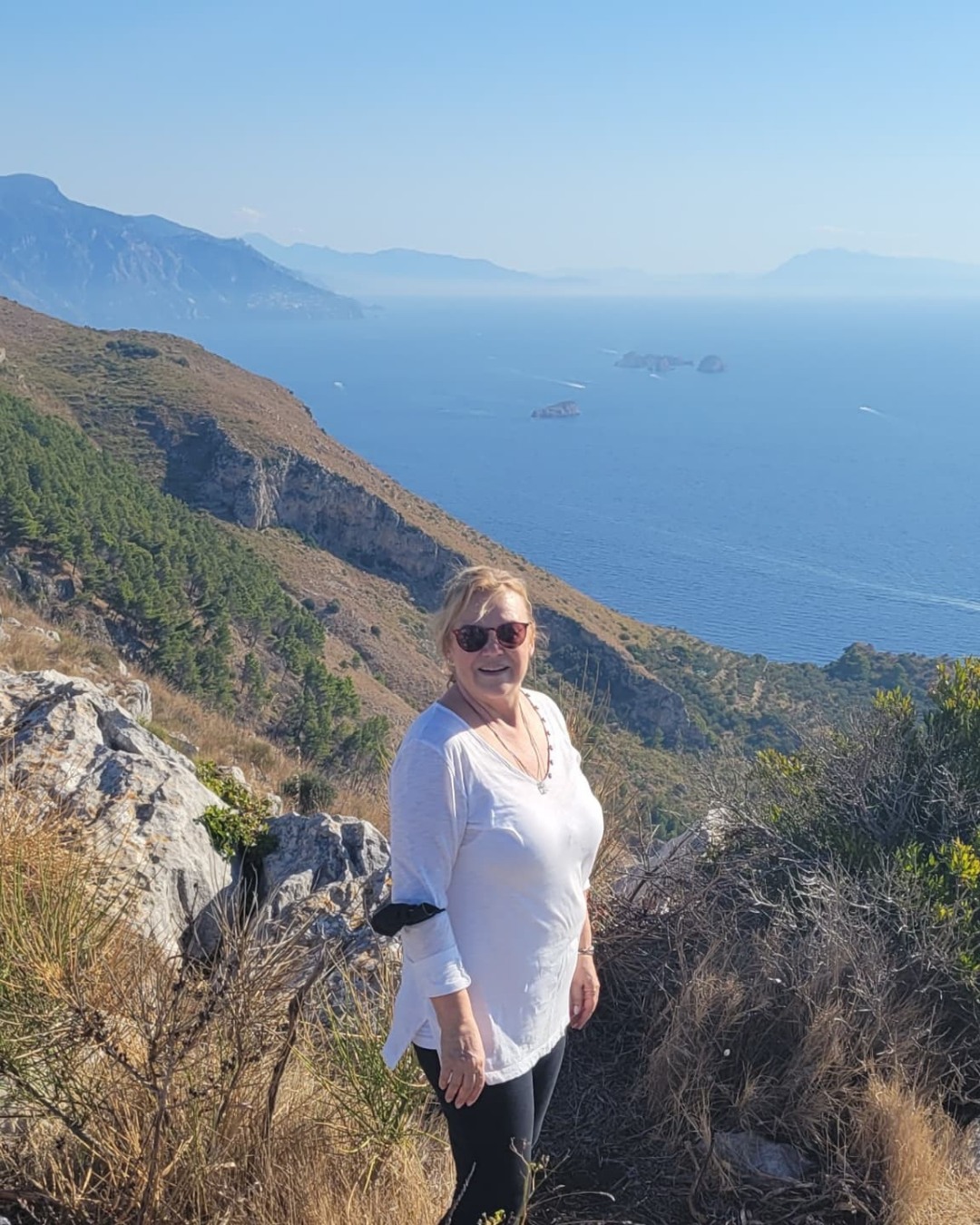 Jolene McDonough standing on a coastal hiking trail with the sea and cliffs behind her