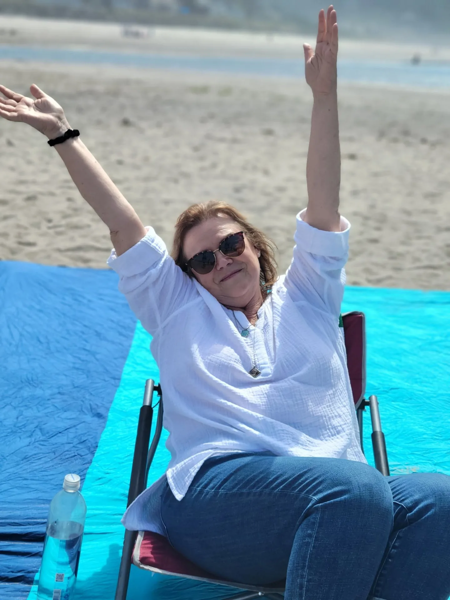 Jolene McDonough sitting on a beach with her arms raised in celebration