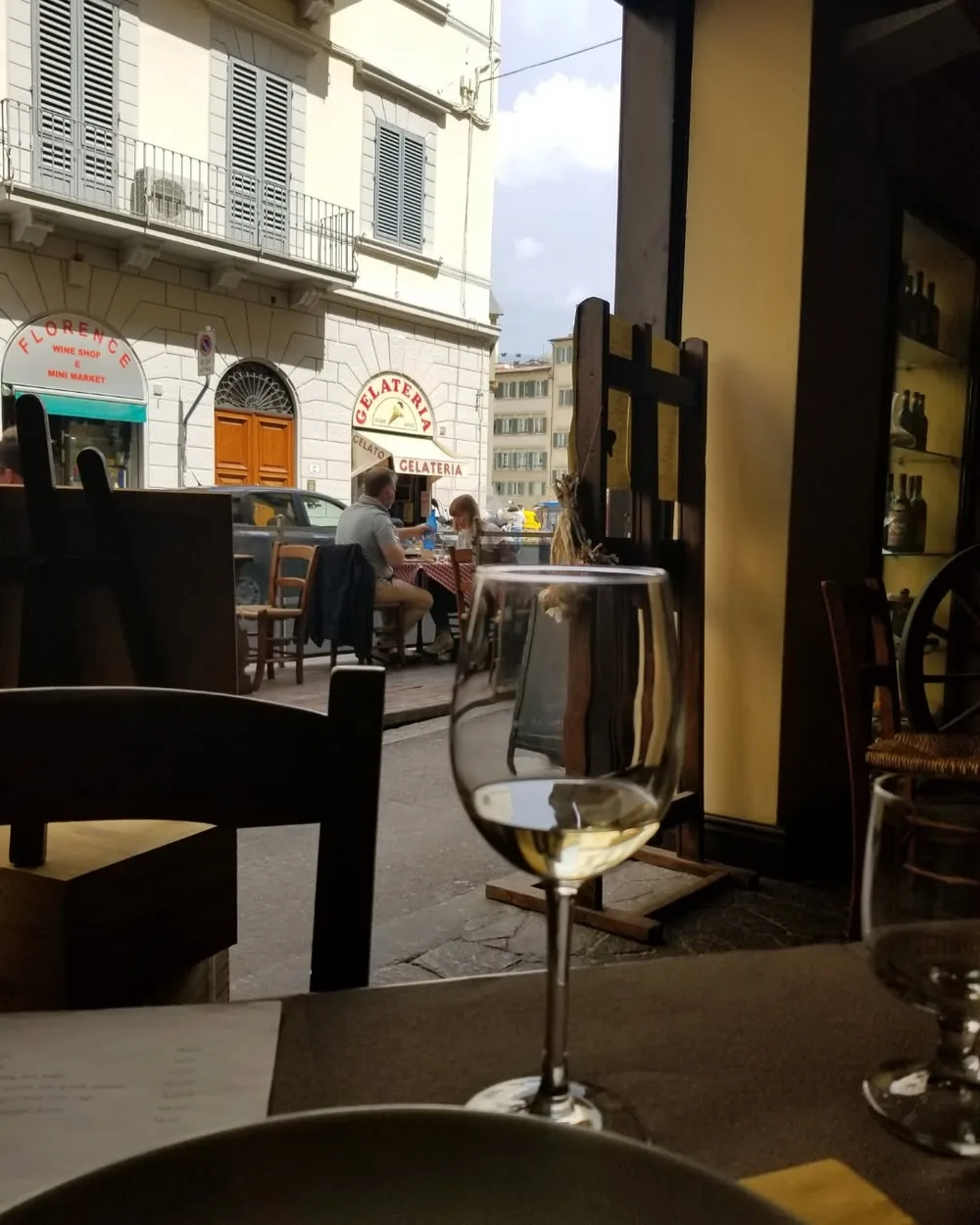 A glass of white wine on a table beside an open Italian street